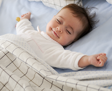 A baby is laying in bed with his arms spread out.